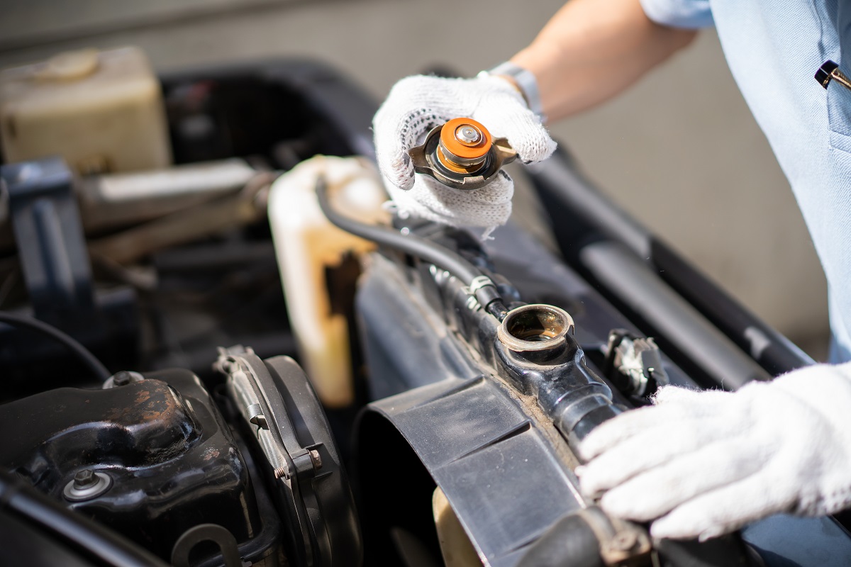 Car repair man checking the coolant system, boiler tank, in the old car.